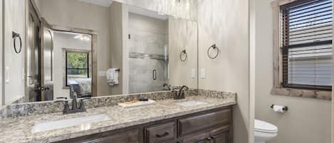 A bathroom with a granite countertop, a large mirror, a sink, and a toilet.
