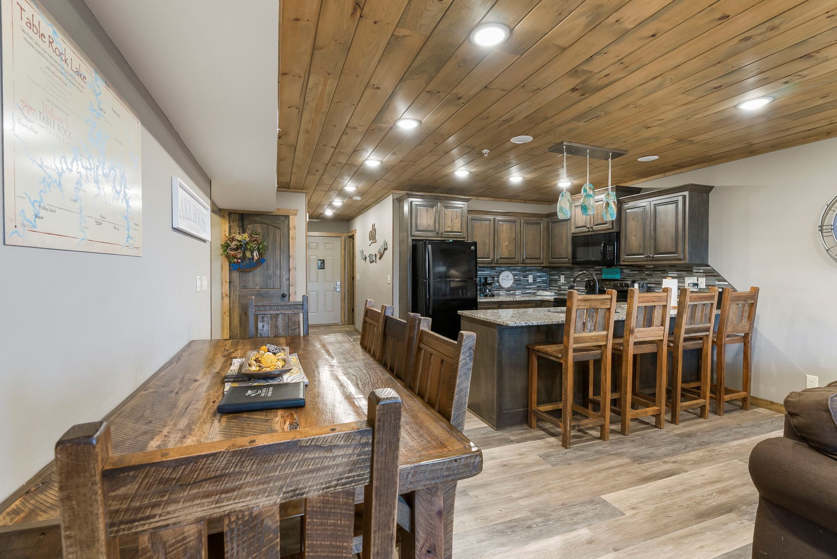A modern kitchen with wooden cabinetry, a central island with bar stools, and a dining area with a long wooden table.