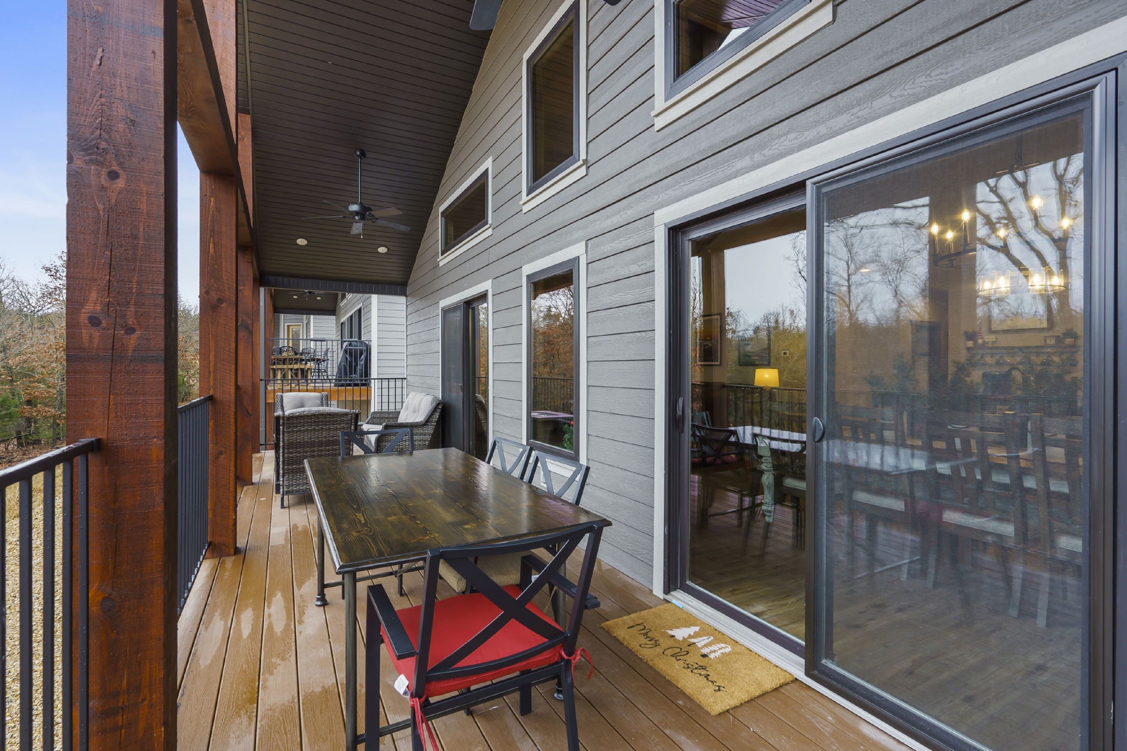 A covered deck with a dining table and chairs, large sliding glass doors, and a ceiling fan.