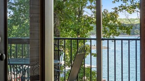 Un balcon avec une table et des chaises, donnant sur une étendue d’eau et des arbres.