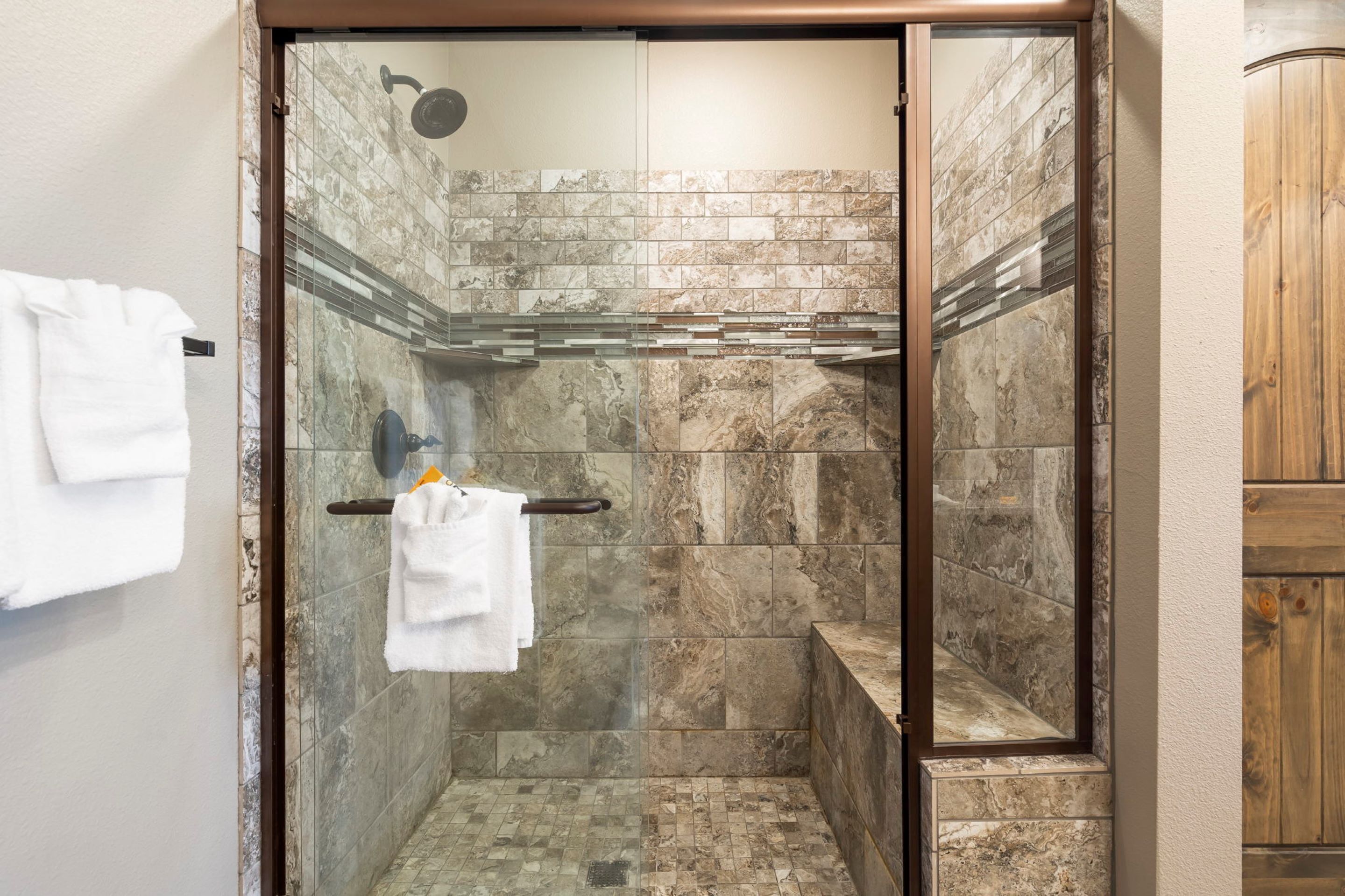 Une douche fermée par des parois de verre, avec un mur en marbre et un meuble en bois.