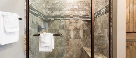 A glass-enclosed shower with a marble wall and a wooden cabinet.