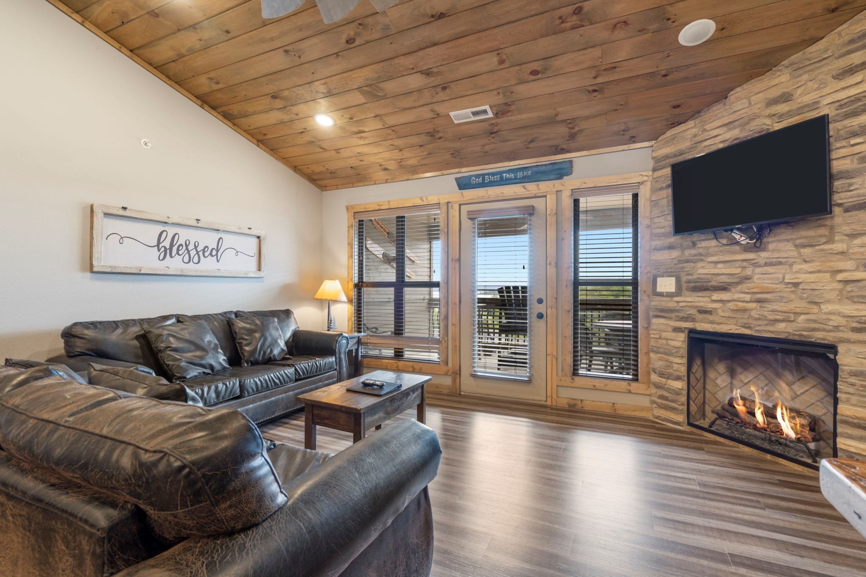 A living room with a leather sofa, a coffee table, a fireplace, and a television mounted on a stone wall.