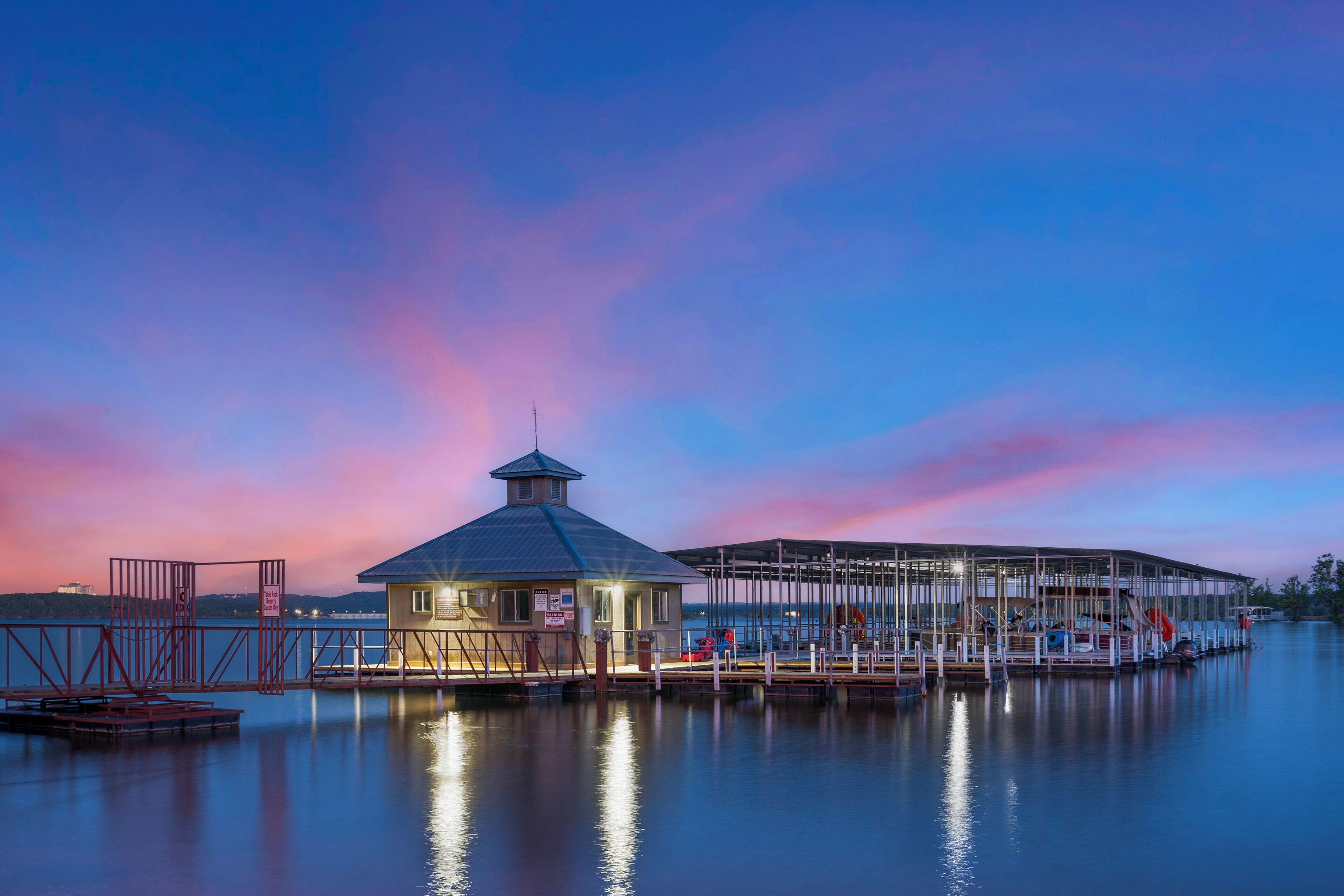A waterfront dock with a small building, possibly a boathouse, and a covered area with boats.