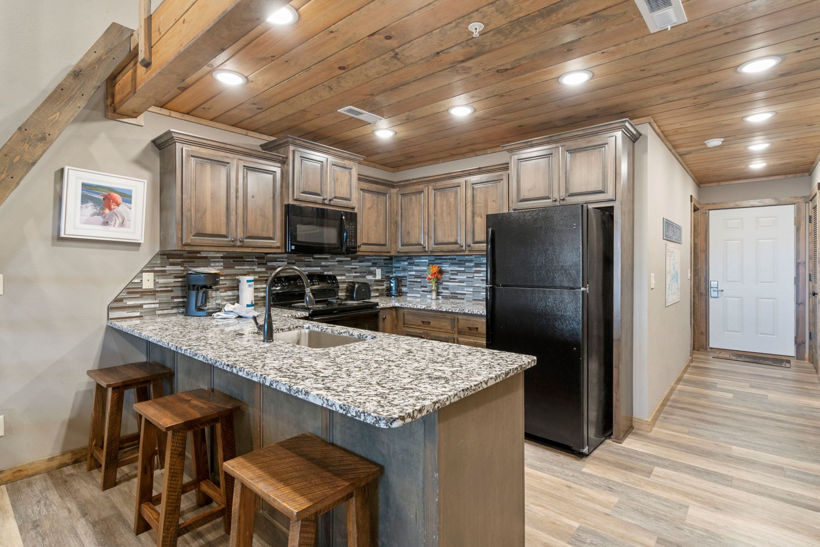A kitchen with wooden cabinets, a granite countertop, a black refrigerator, and a built-in microwave.