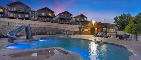 A pool area with a slide, lounge chairs, and a view of the buildings in the background.