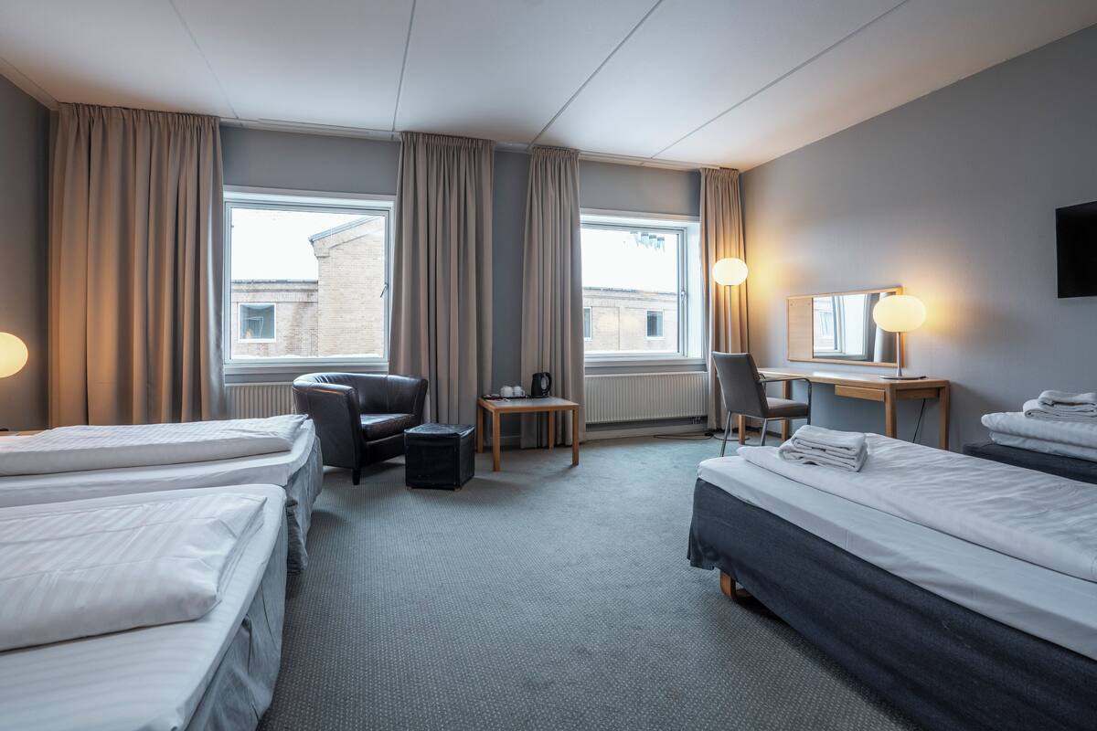 Et hotelværelse med to senge, et skrivebord, en stol, et lille bord og en radiator.