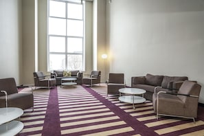 Een moderne zithoek met een gestreept tapijt, diverse zitplaatsen waaronder banken en fauteuils, en een groot raam dat voor natuurlijk licht zorgt.