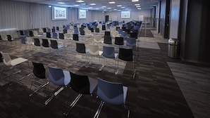 A conference room with rows of chairs, a carpeted floor, and a projector screen.
