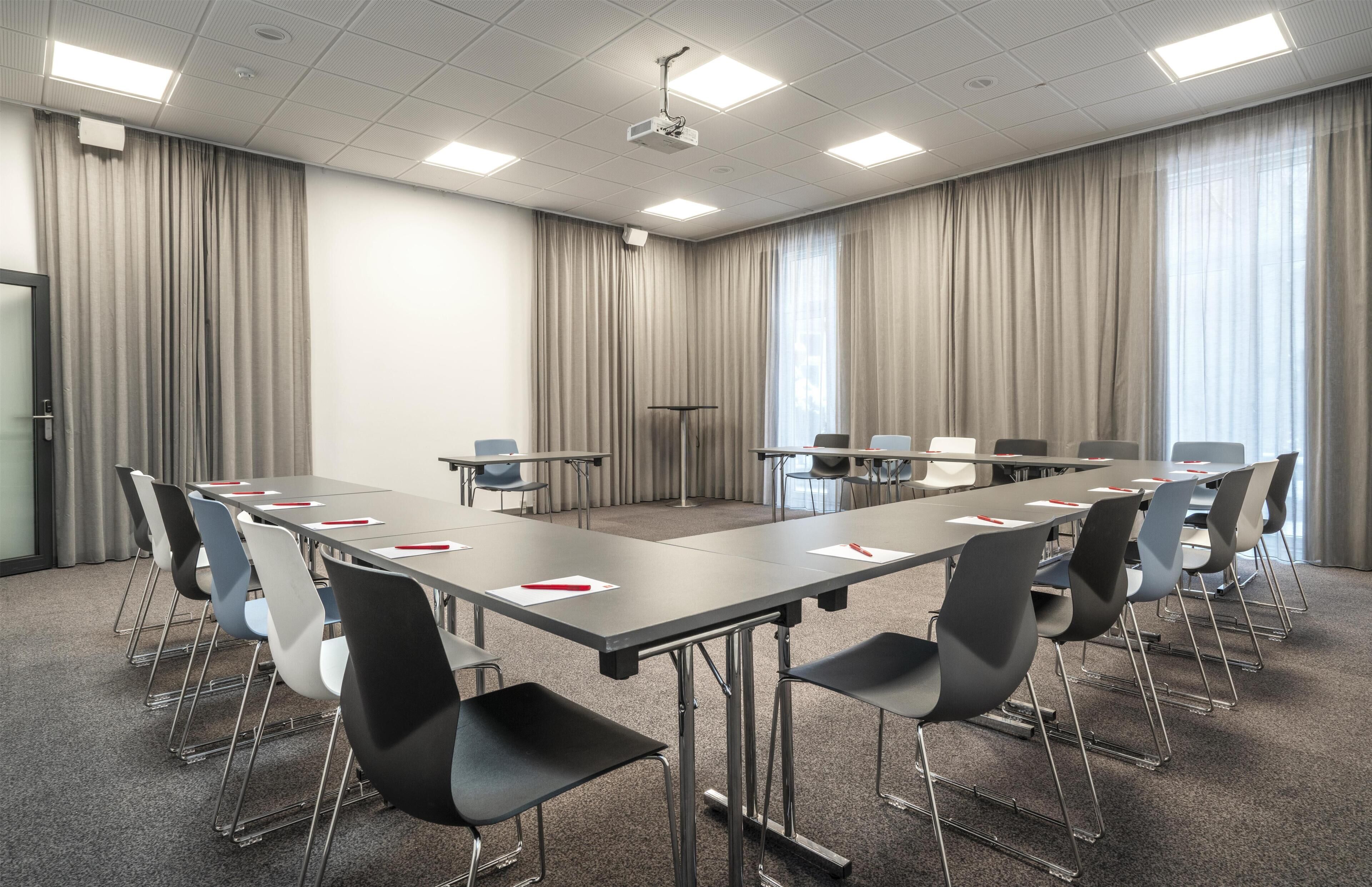A conference room with a long table, chairs, a projector, and curtains.