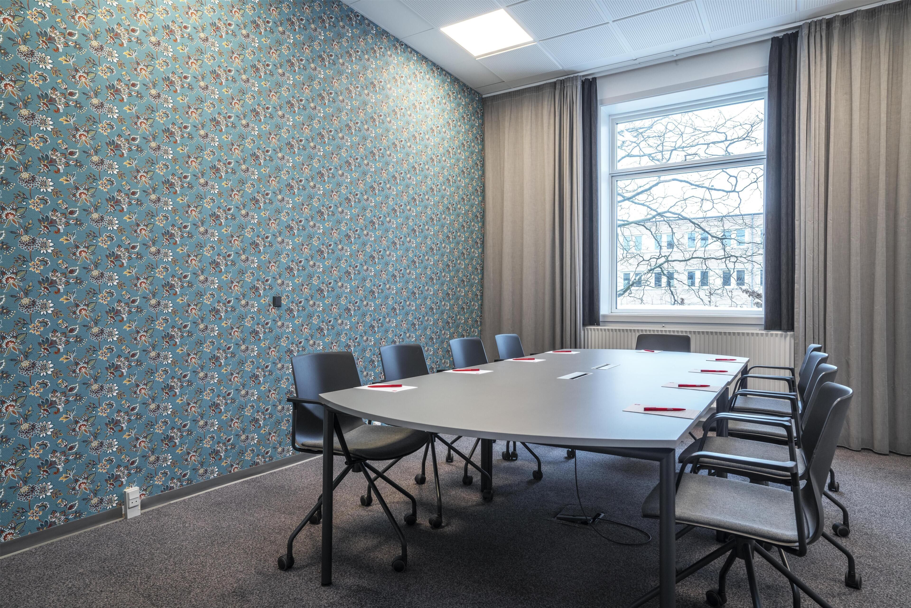 A conference room with a floral wallpaper, a large table with chairs, and a window with a view of buildings.