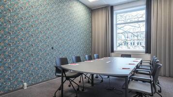 A conference room with a floral wallpaper, a large table with chairs, and a window with a view of buildings.