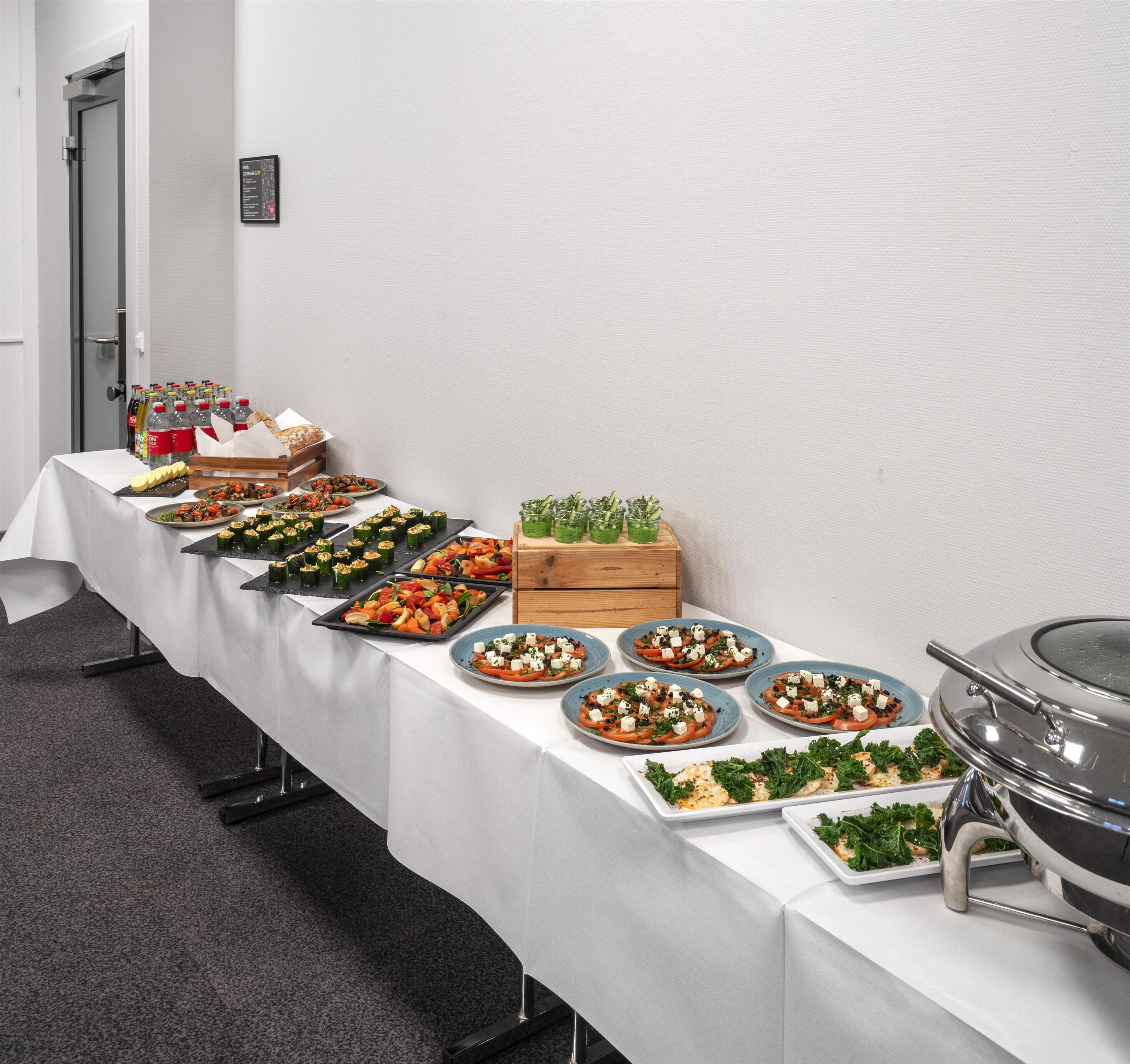 Mesa de buffet com diversos pratos, incluindo saladas, legumes e uma estação de grelhados.