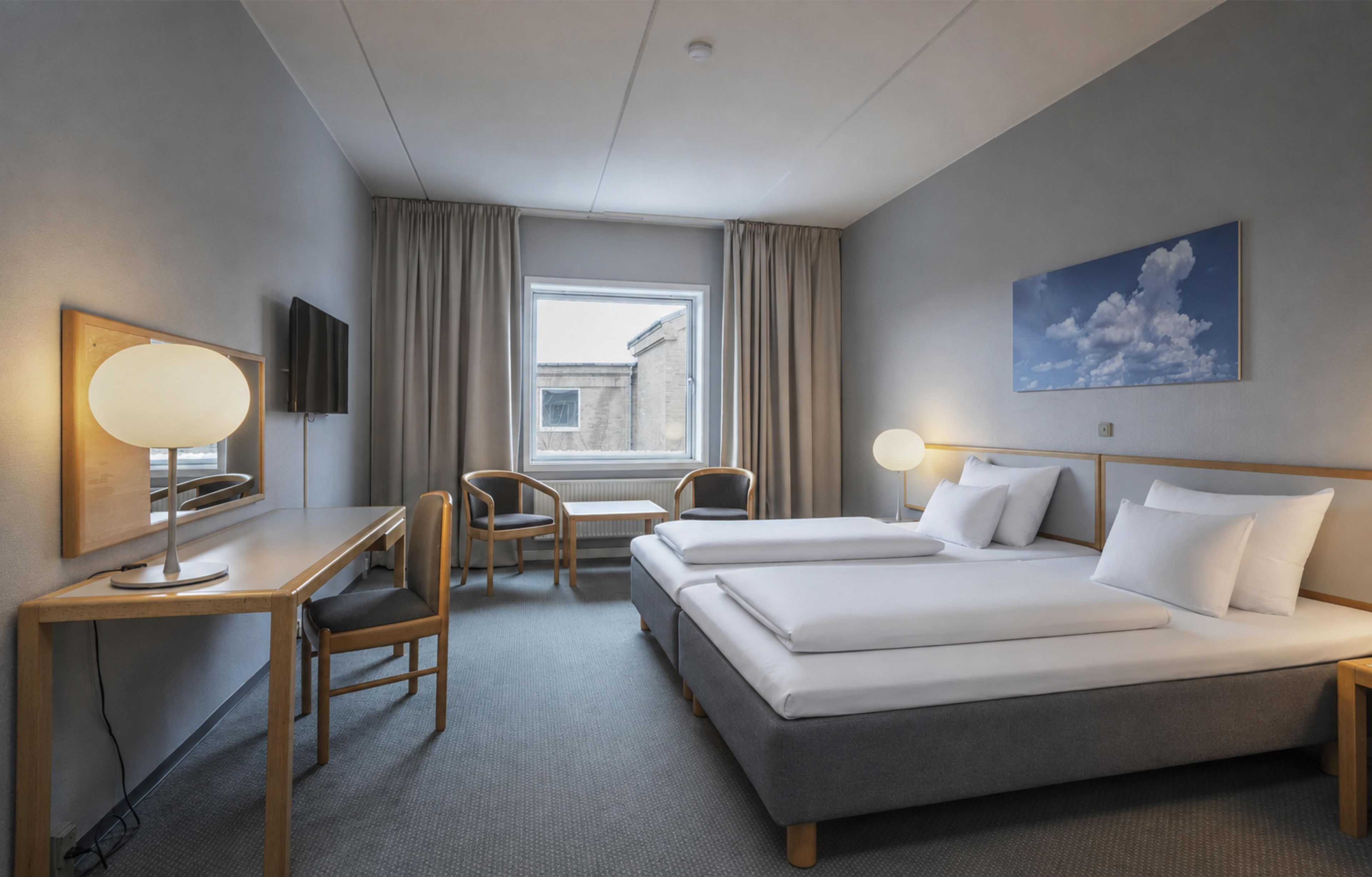 A hotel room with a bed, a desk, a chair, a television, and a window with curtains.