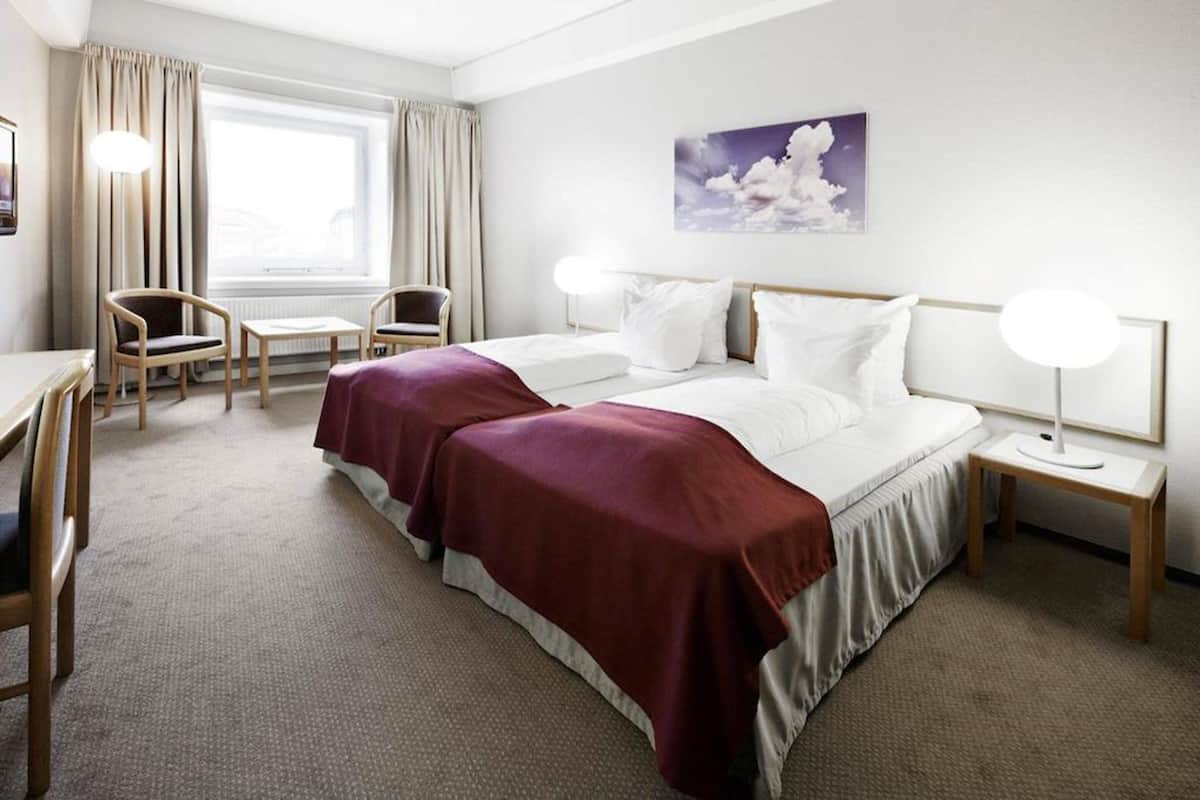 A hotel room with a large bed, two bedside tables, a desk, and a chair.