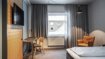 Une chambre d’hôtel avec un lit, un bureau, une chaise, une télévision et une fenêtre avec des rideaux.