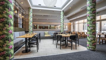 Restaurante com pé-direito alto, janelas amplas e colunas florais tropicais.