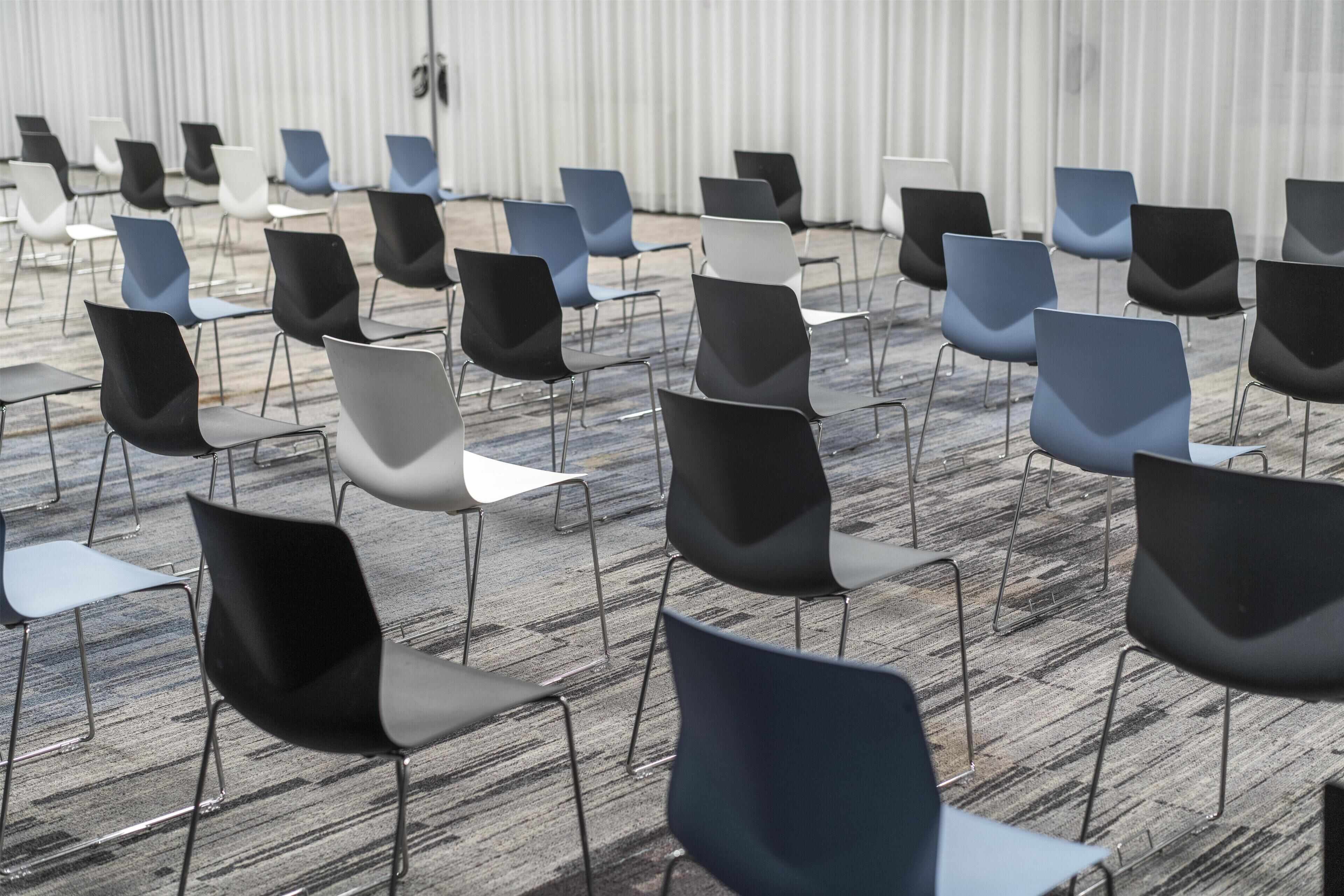 Rows of chairs arranged in a conference room with a carpeted floor and a plain wall in the background.