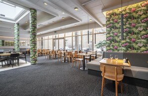 A modern dining area with high ceilings, large windows, and tropical floral wall decor.