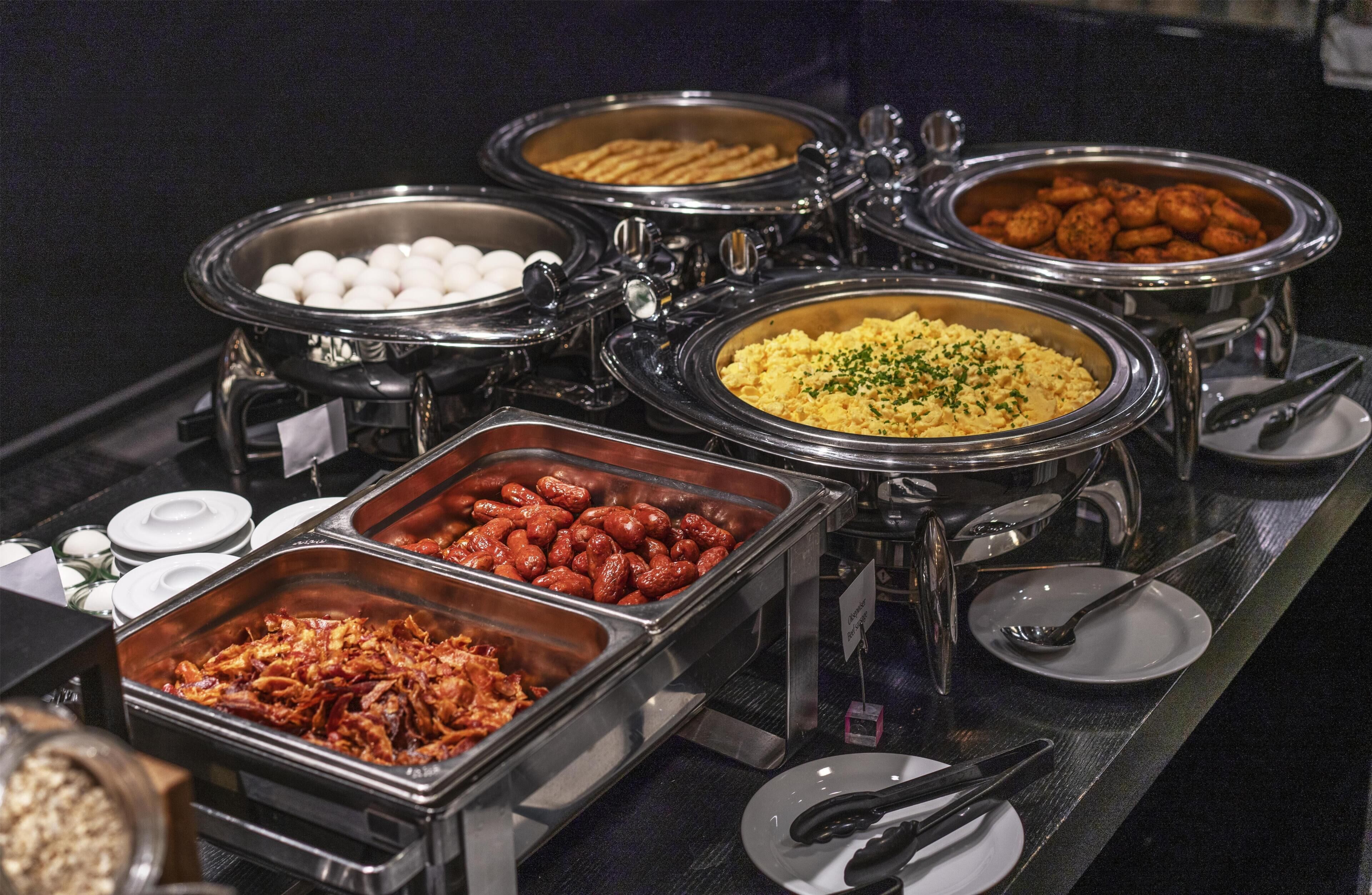 Un bufé con diferentes alimentos en recipientes metálicos.
