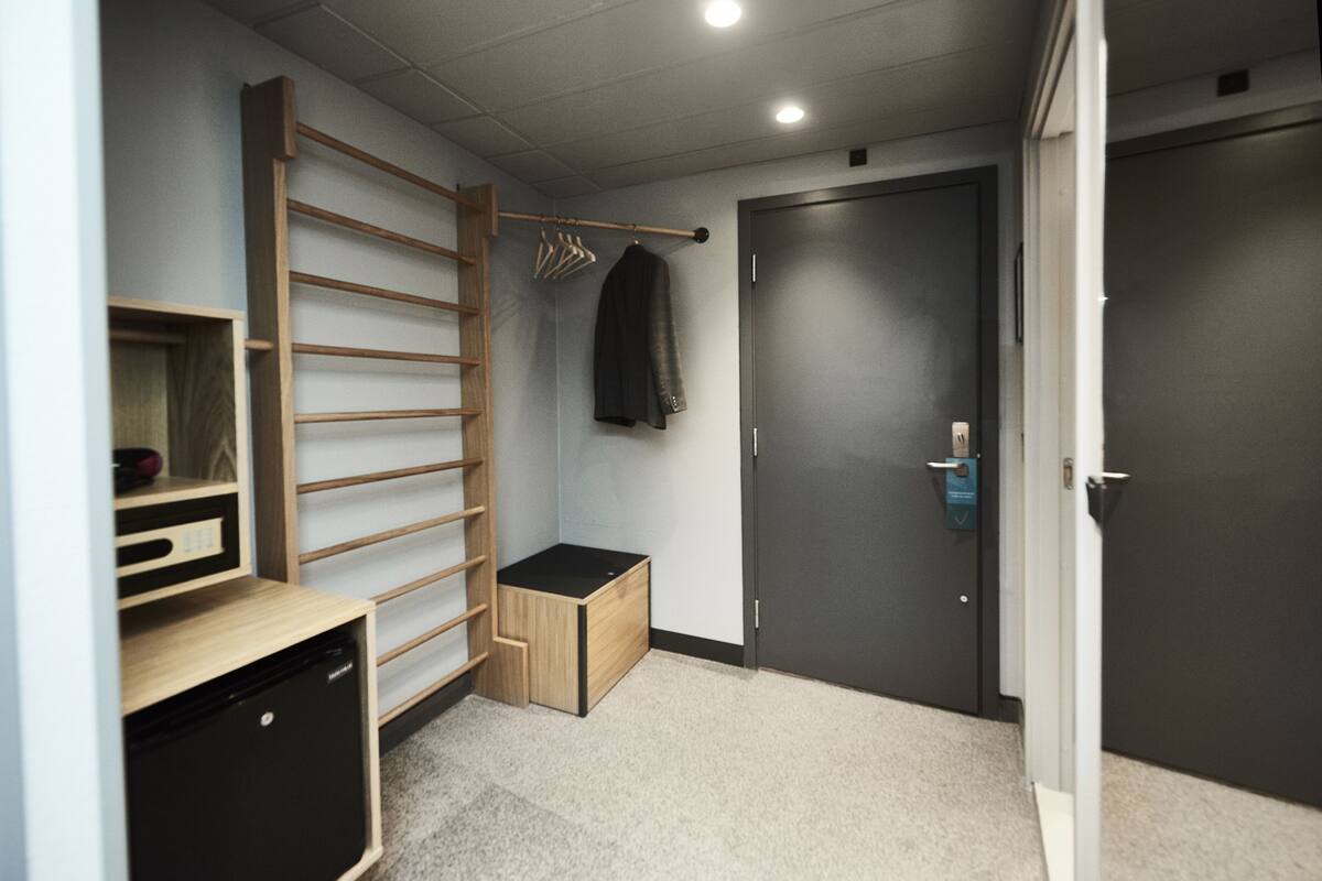 A compact room with a built-in wardrobe, a small wooden cabinet, and a door with a security lock.