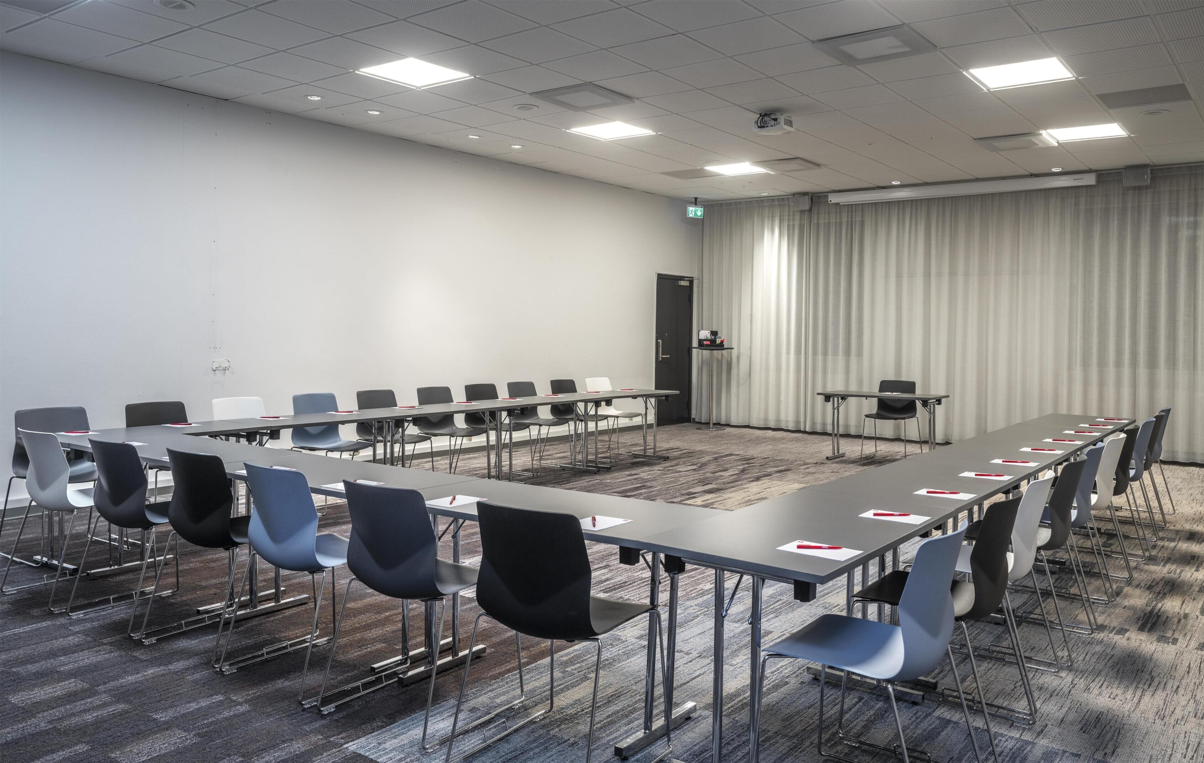 Een vergaderruimte met een lange tafel, stoelen en een vloerkleed.