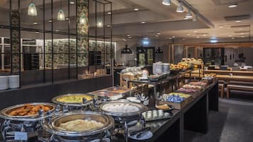 Área de buffet com diversas opções de comida e um espaço de estar ao fundo.