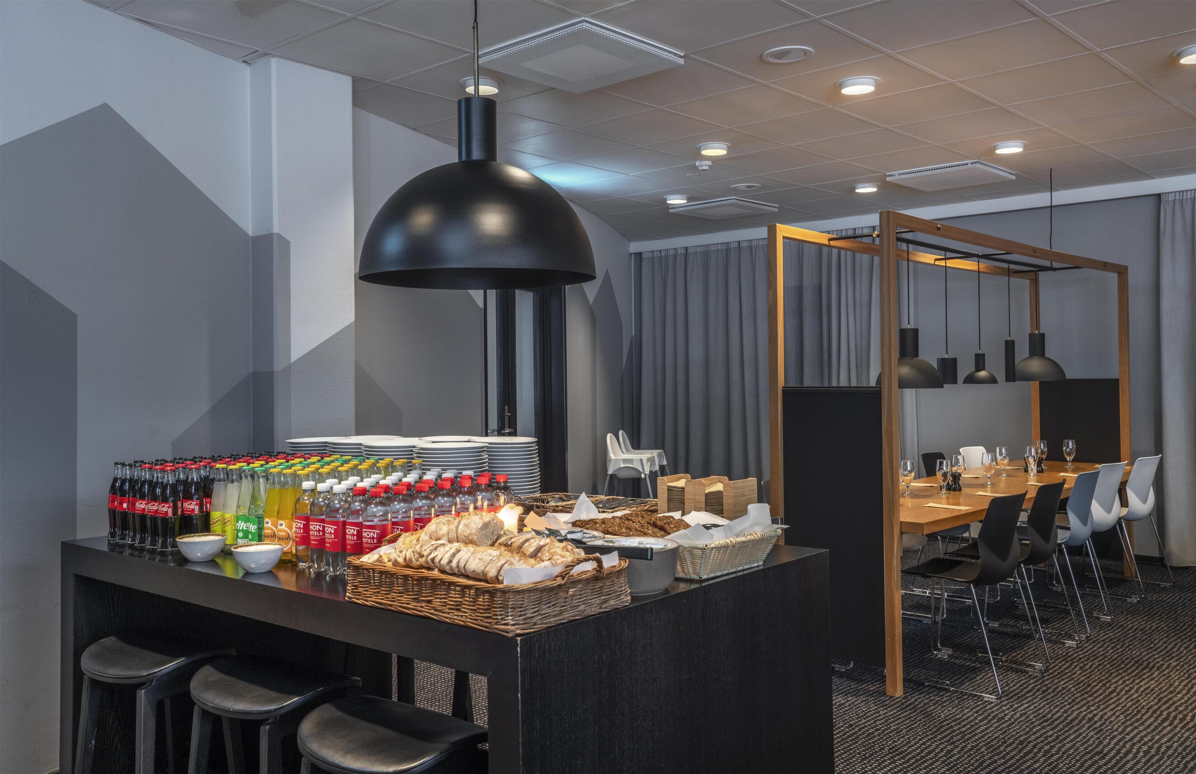 A modern hotel room with a breakfast bar, seating area, and a large window with curtains.