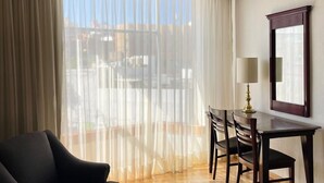 A hotel room with a bed, a desk, and a chair. There is a large window with curtains, a lamp on the desk, and a mirror on the wall. - Hotel Arroyo de la Plata (Zacatecas)