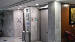 An elevator area with a marble wall, a trash bin, and a red chair. - Hotel Arroyo de la Plata (Zacatecas)