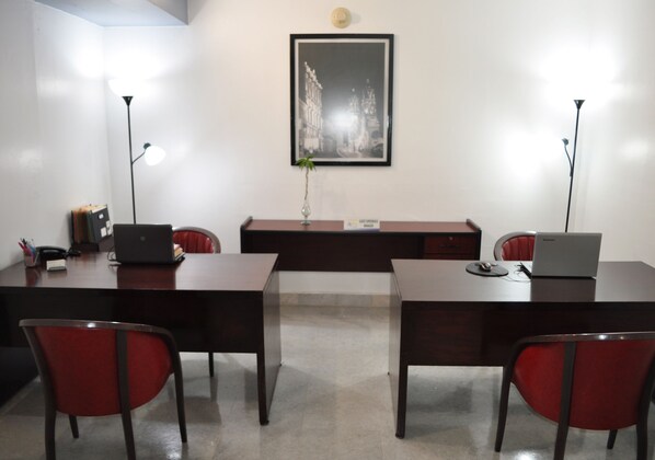 Un salón de conferencias con dos escritorios, sillas rojas, un cuadro en la pared y dos lámparas de pie.