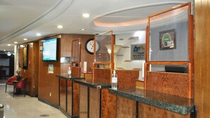 A hotel reception area with wooden reception desks, a clock, and a digital screen displaying information. - Hotel Arroyo de la Plata (Zacatecas)