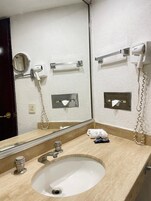 Baño con lavamanos, espejo, secador de pelo y dispensador de toallas.
