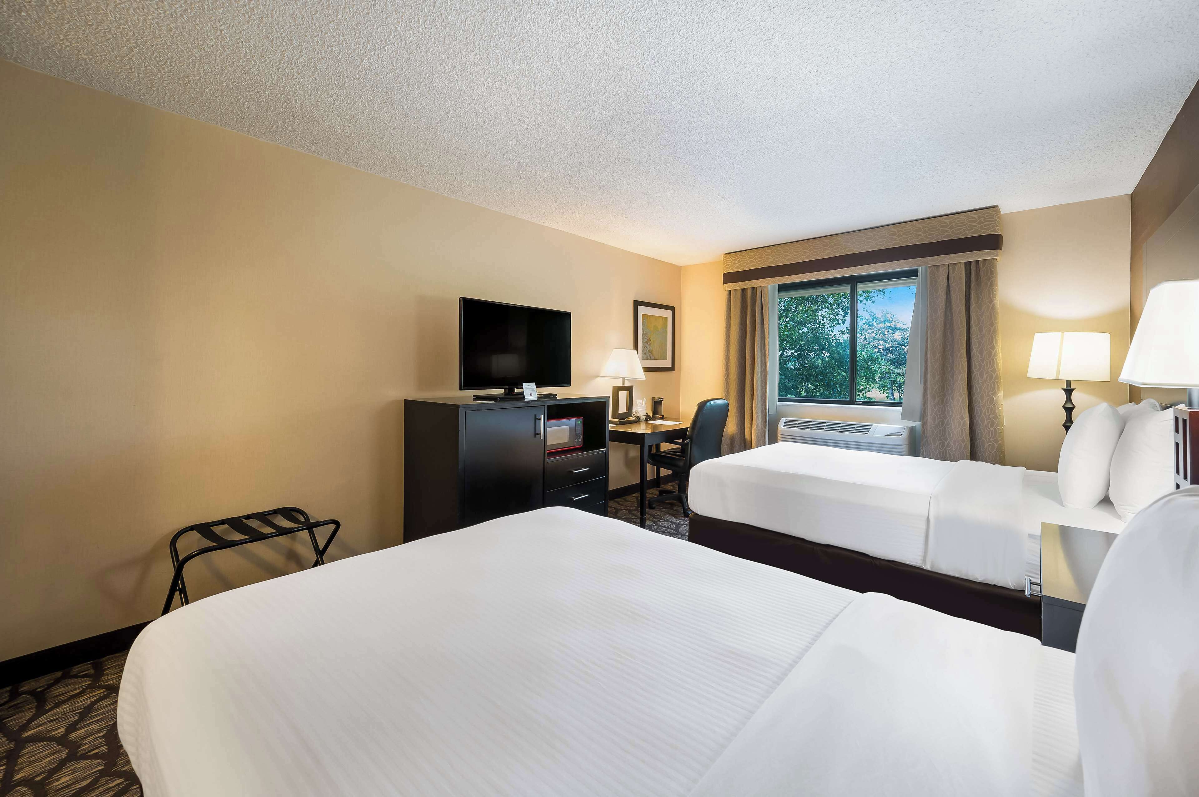 A hotel room with two beds, a desk with a TV, a chair, and a window with curtains.