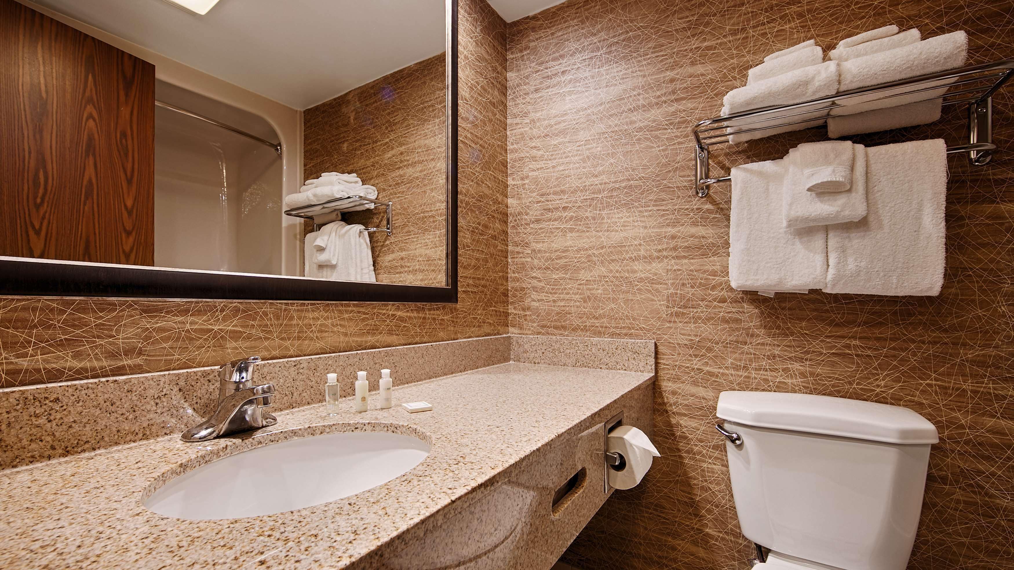 A bathroom with a granite sink, a toilet, and a towel rack with folded towels.