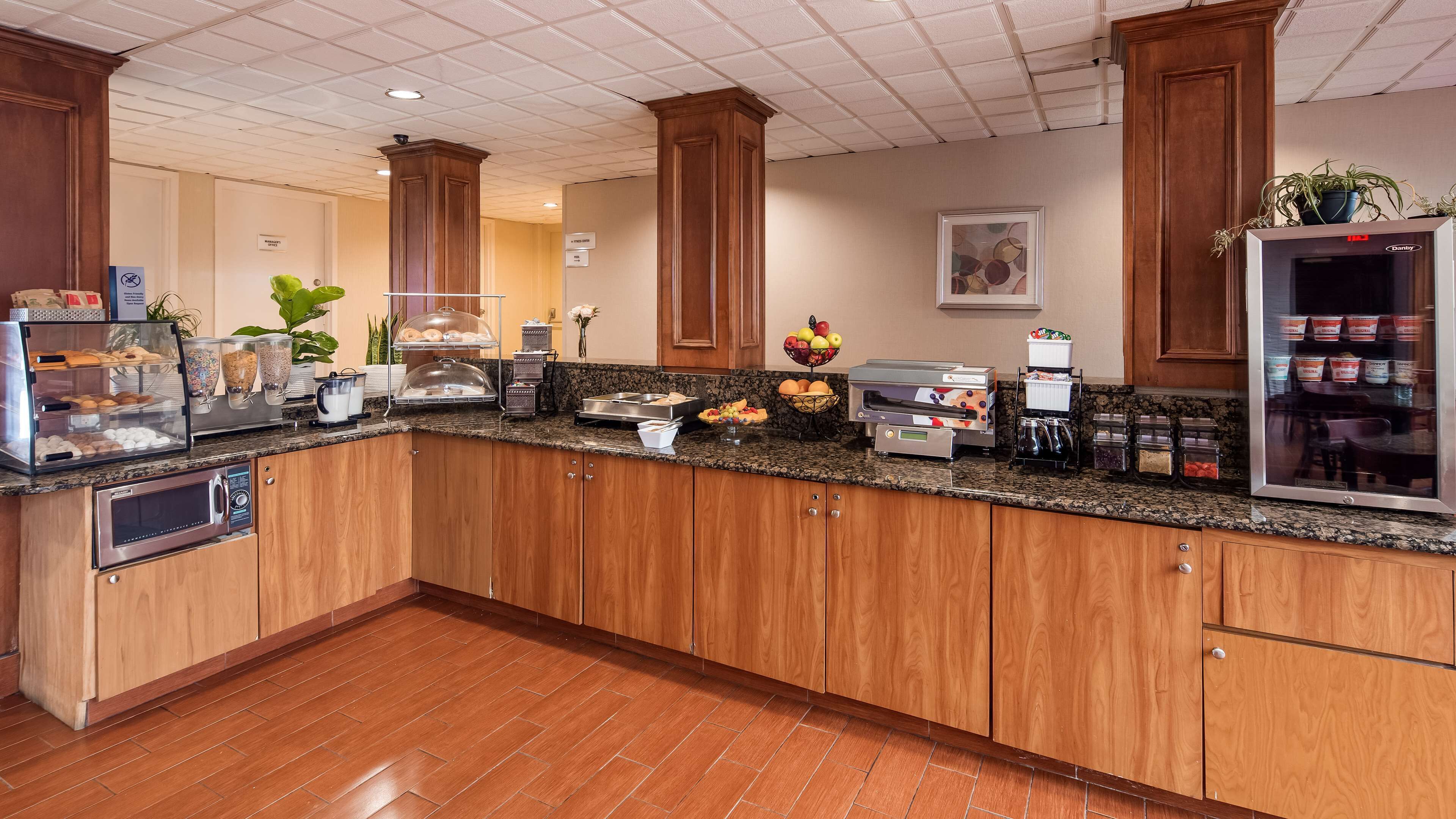 A hotel kitchen with a granite countertop, wooden cabinets, a coffee station, and a fruit bowl.