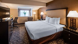 A hotel room with a large bed, a desk with a computer, a chair, a window with curtains, and two bedside lamps. - Best Western Detroit Livonia (Livonia)