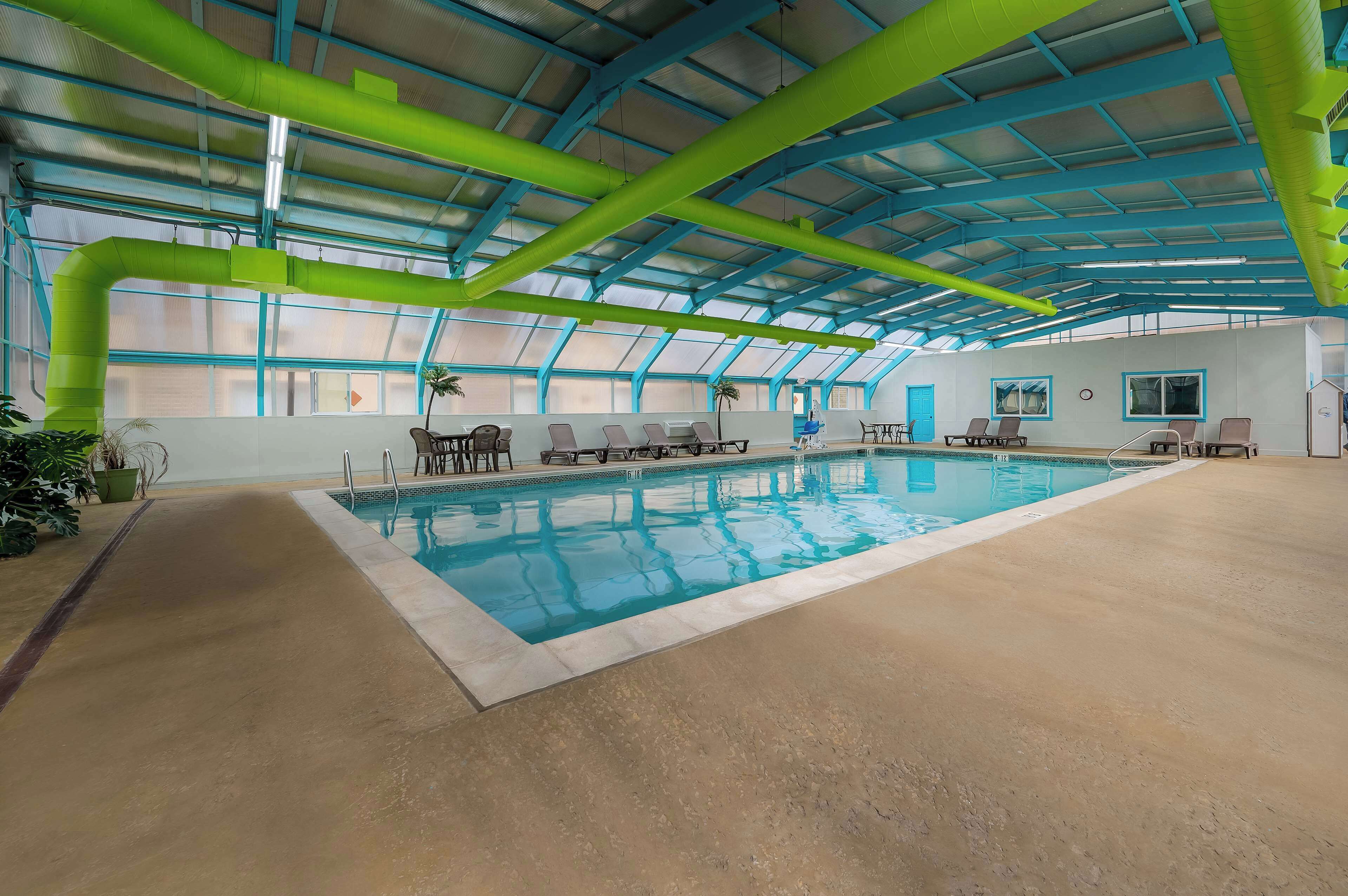 An indoor swimming pool with a high ceiling, clear glass panels, and lounge chairs along the poolside.