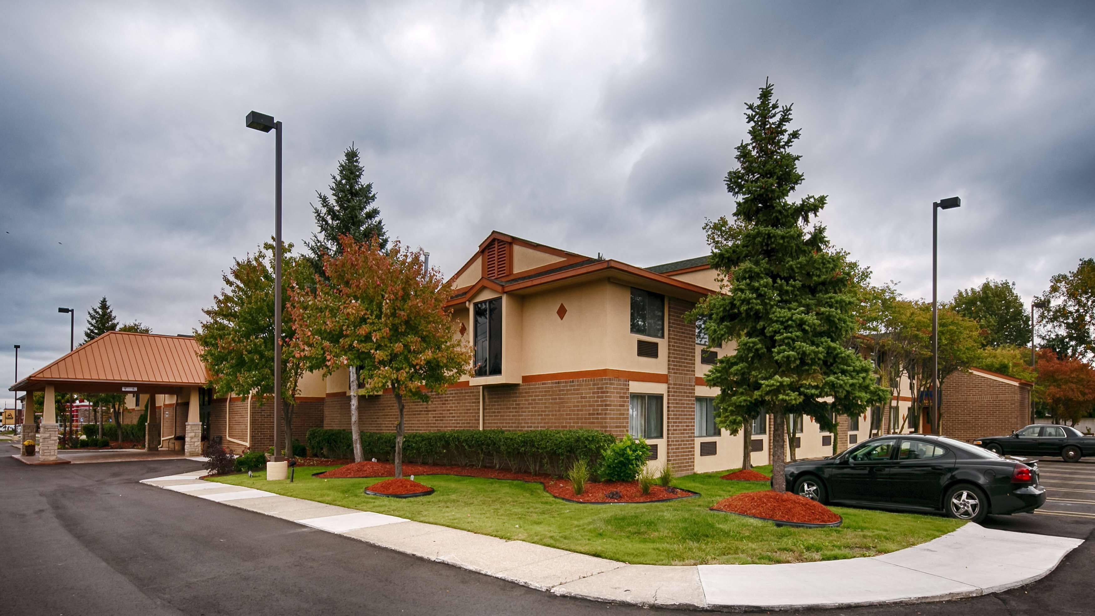 A two-story building with a brick facade and a flat roof. There are landscaped areas with trees and shrubs in front of the building.