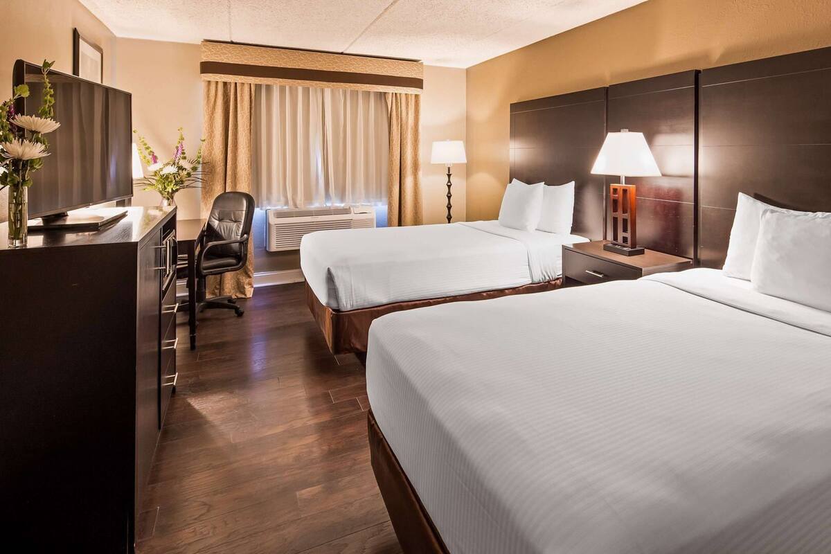 A hotel room with two beds, a desk, a chair, a TV, and a window with curtains.