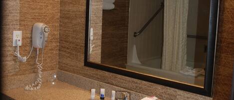 A bathroom with a sink, mirror, hairdryer, and towel rack.