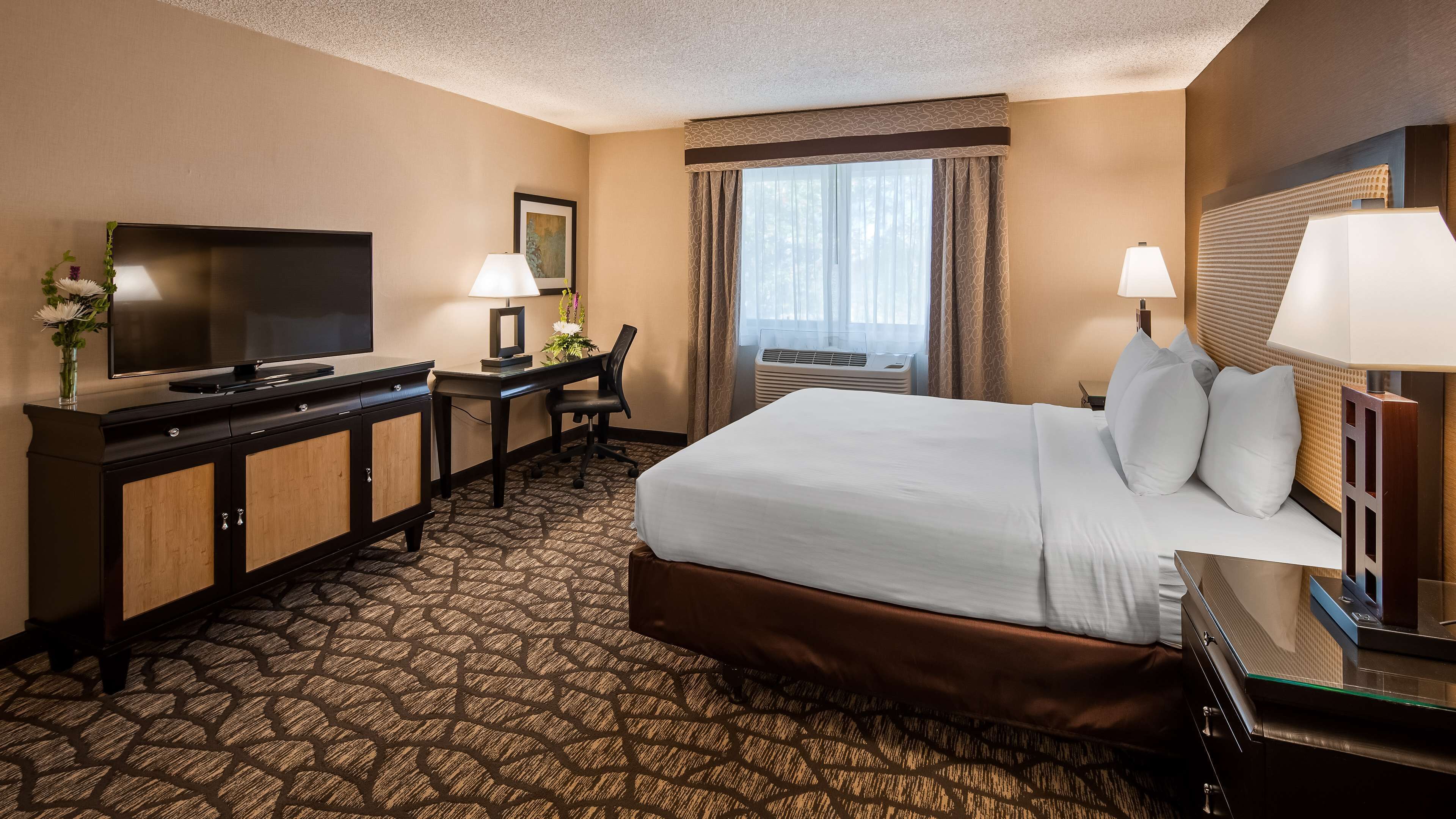 A hotel room with a bed, a desk, a TV, a chair, and a window with curtains.