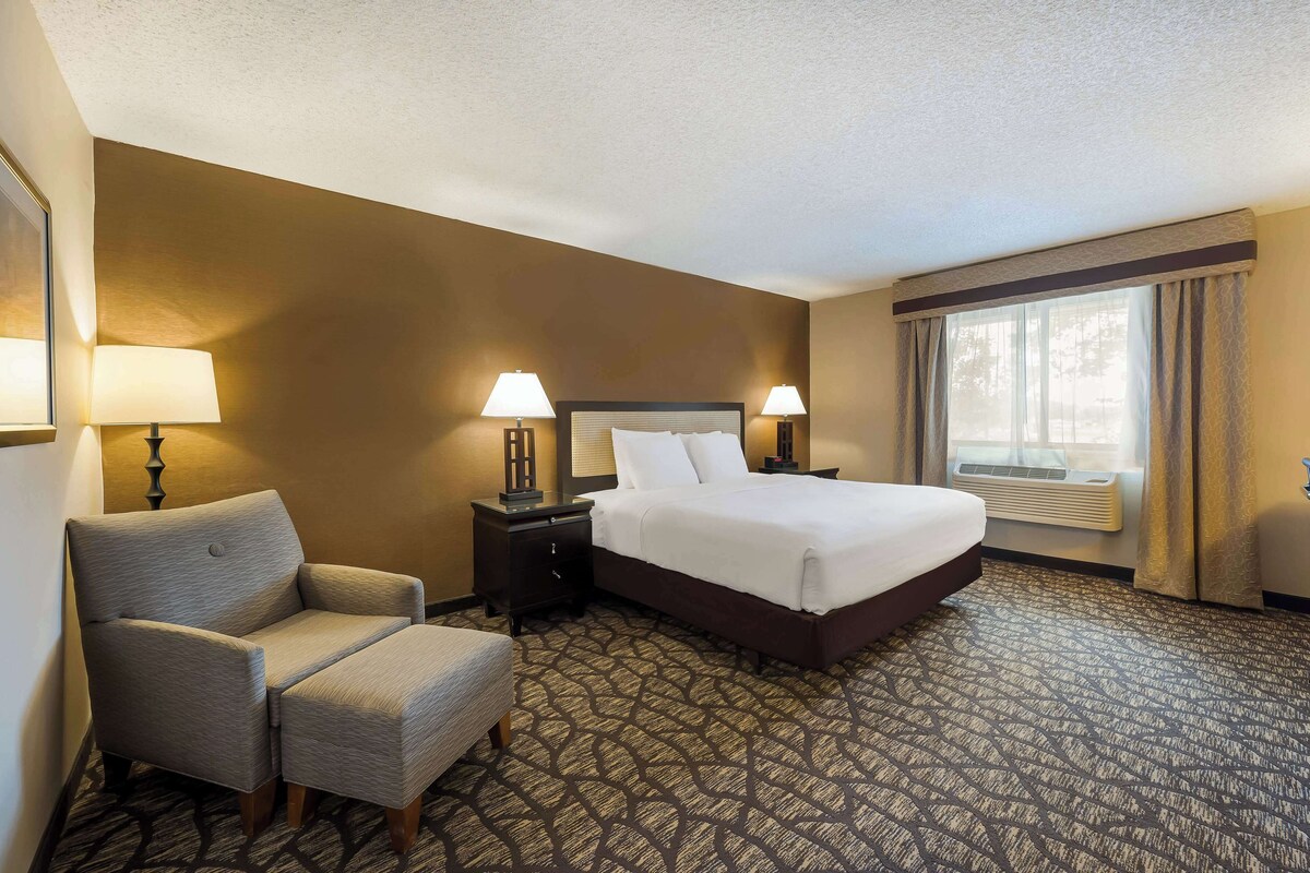 A hotel room with a bed, two bedside tables with lamps, a chair, and a patterned carpet.