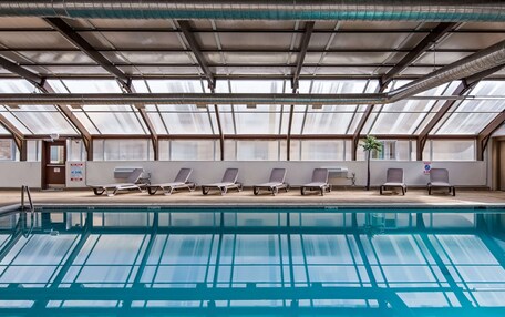 A swimming pool with lounge chairs and a glass ceiling.