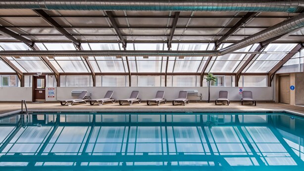 A swimming pool with lounge chairs and a glass ceiling. - Best Western Detroit Livonia (Livonia)