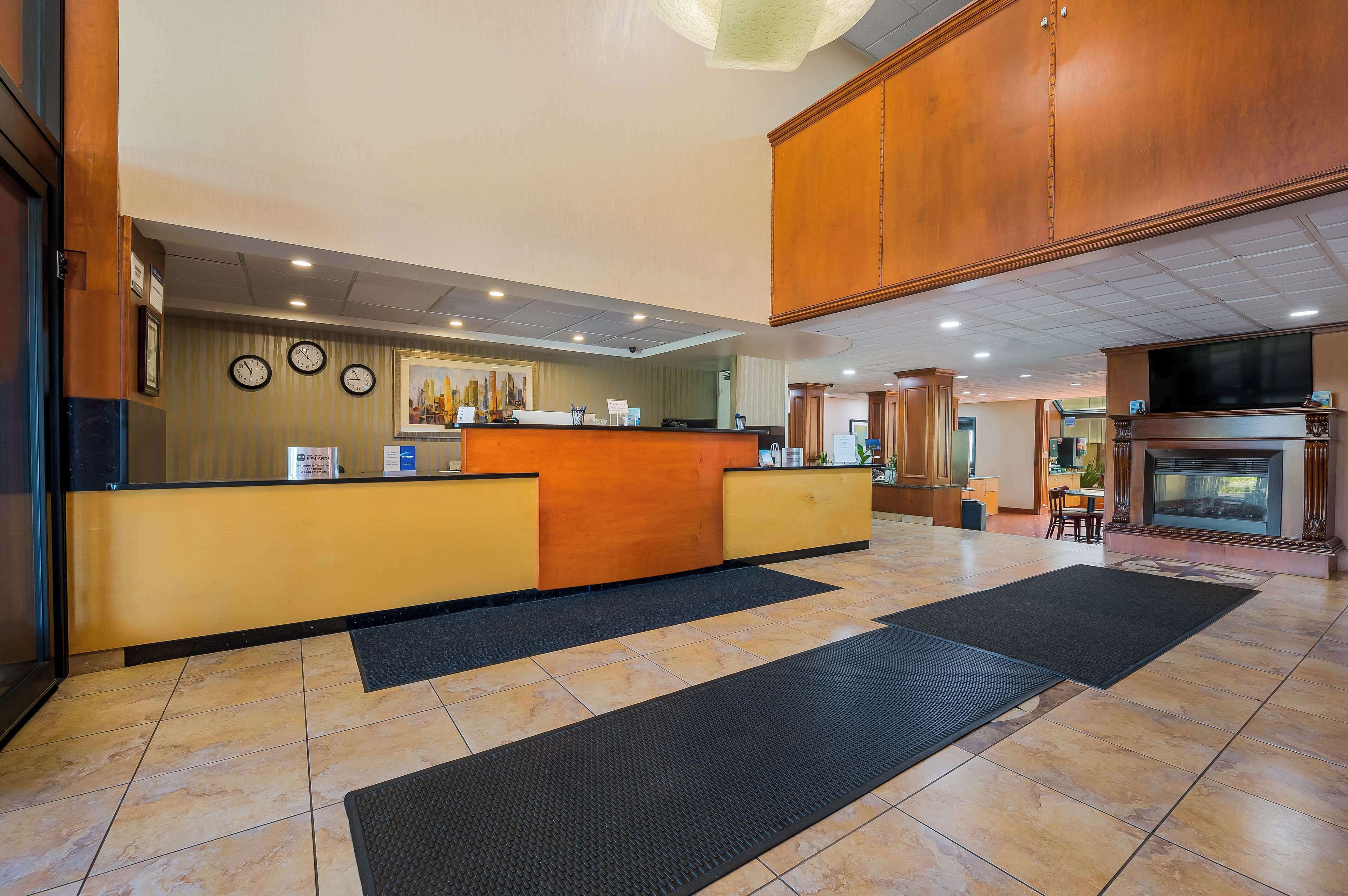 A hotel reception area with a wooden reception desk, multiple clocks on the wall, and a fireplace in the background.