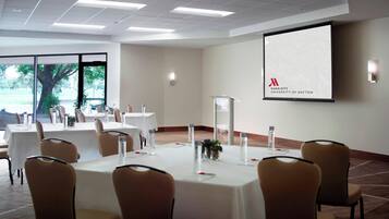 A conference room with tables and chairs, a projector screen displaying the Marriott University of Dayton logo, and a view of trees outside.
