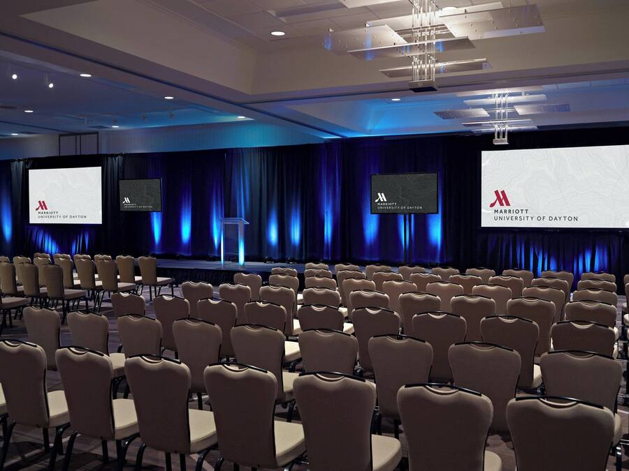 A conference room with rows of chairs, a stage with a podium, and large screens displaying the Marriott University of Dayton logo.