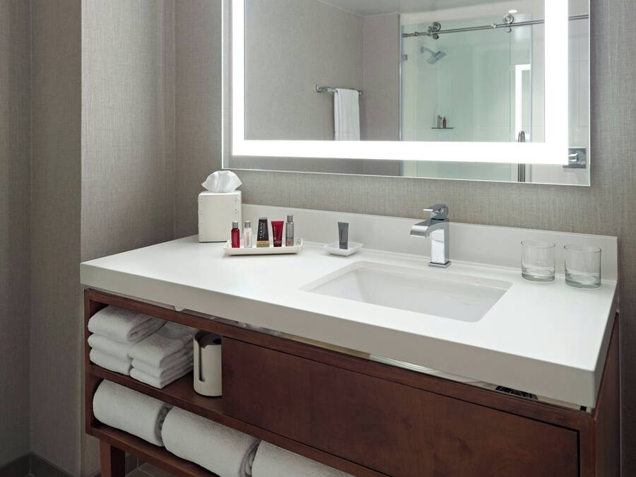 A modern bathroom with a white sink, a large mirror, and a wooden vanity.