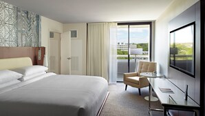 A hotel room with a large bed, a desk with a chair, a TV, and a view of a building through a window. - Marriott at the University of Dayton (Dayton)